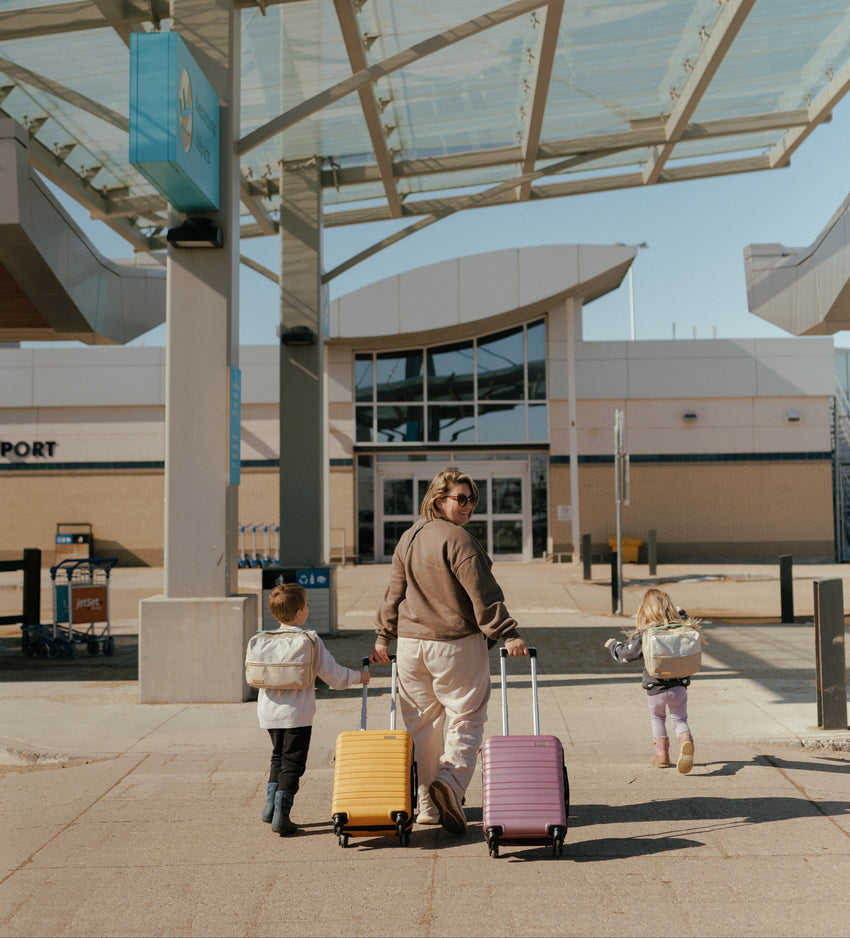 Mom traveling with two young children at the airport with suitcases and Calm & Confident Travel Bags.